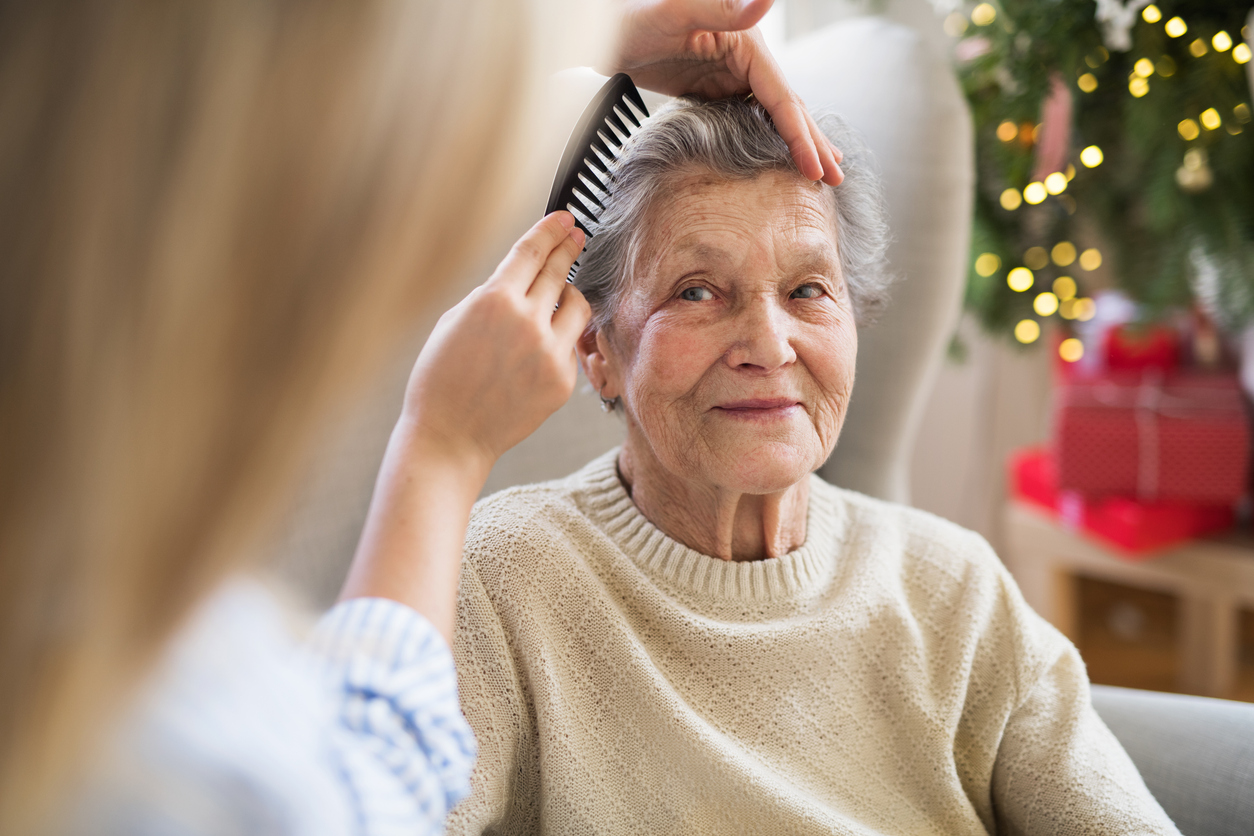 A health visitor combing hair of senior woman at home at Christmas time.